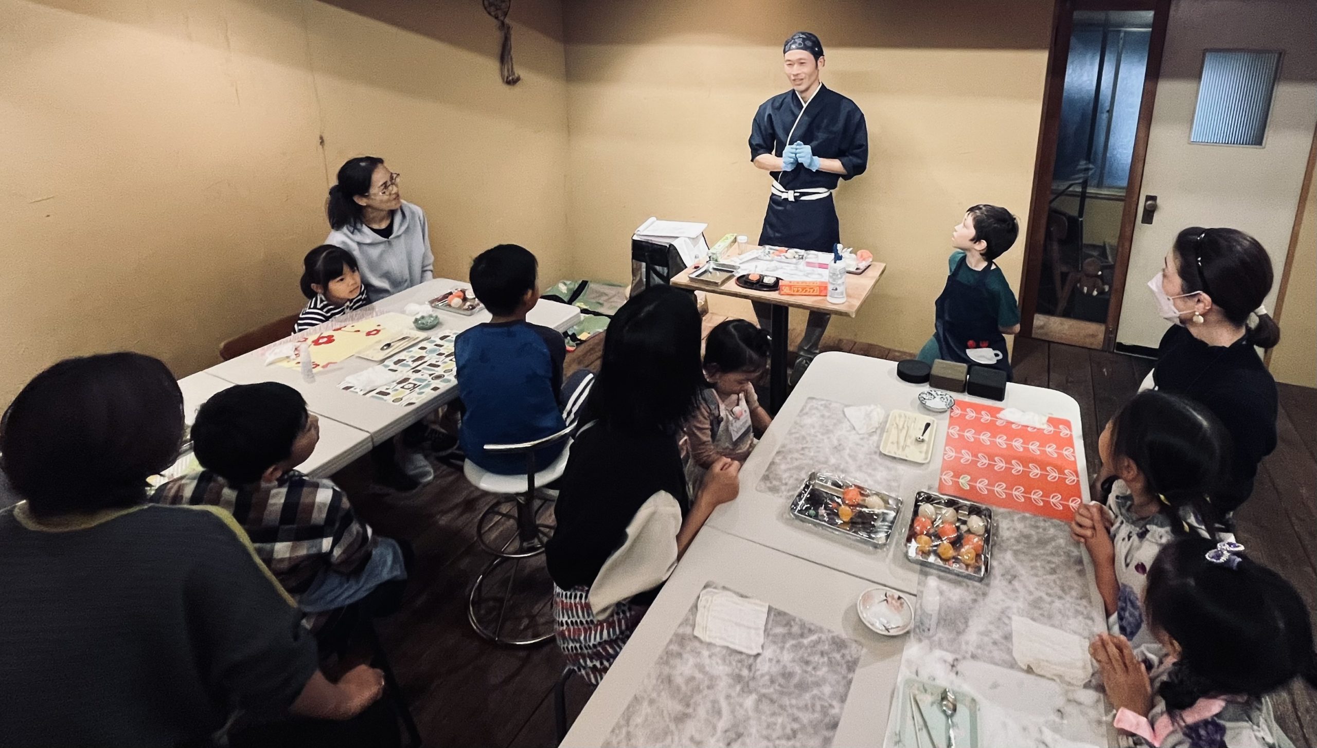 Kenji Wada stands in front of children and parents explaining wagashi.